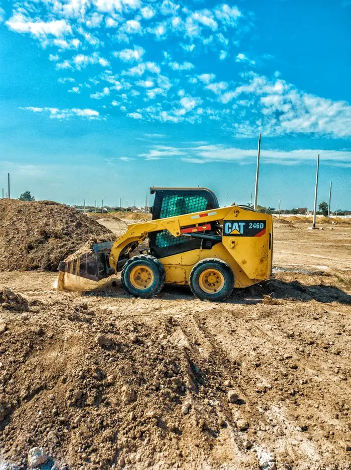 Skid steer loader at a daytime construction site with blue sky backdrop.